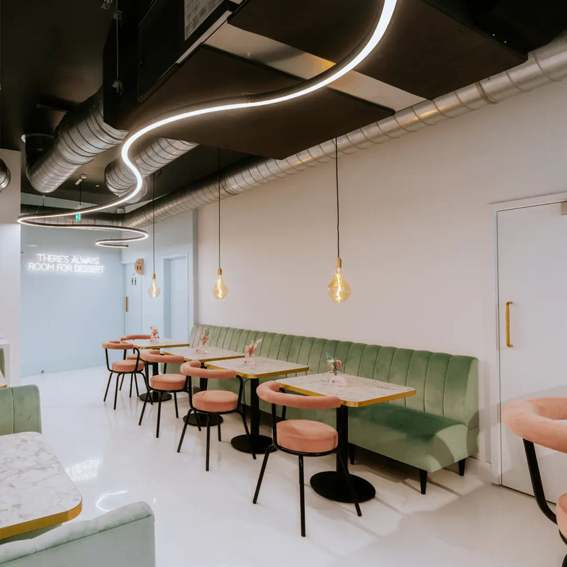 A curved bespoke curved linear wiggle made suspended LED ceiling light in a stylish pink and green cafe.