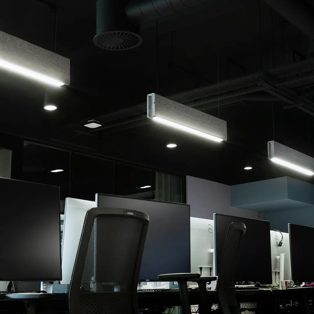 An office space shown with multiple computer screens.  The area is lit with 3 light grey acoustic baffle lights to light the area and reduce background noise.
