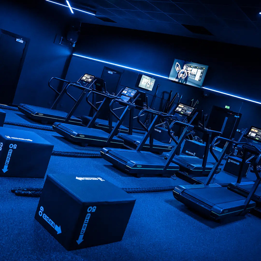 A stylish gyms running machine area with RGBW linear lights set to blue running across the ceiling and bespoke X shaped blue pendants.