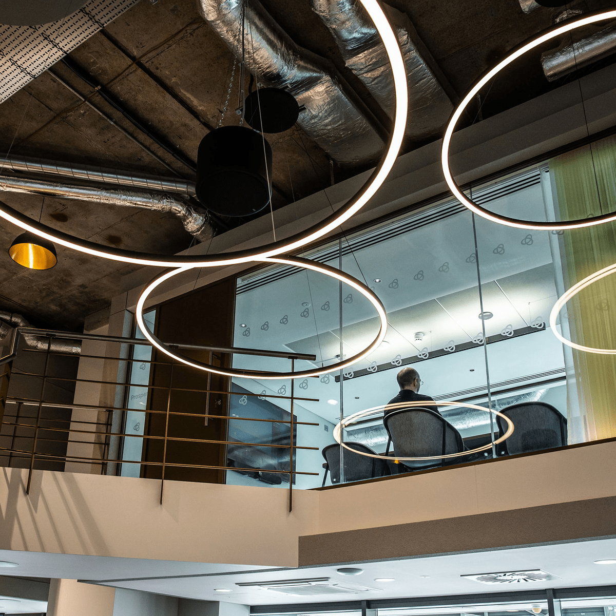 Round extra large halo LED suspended lighting within an industrial style office.