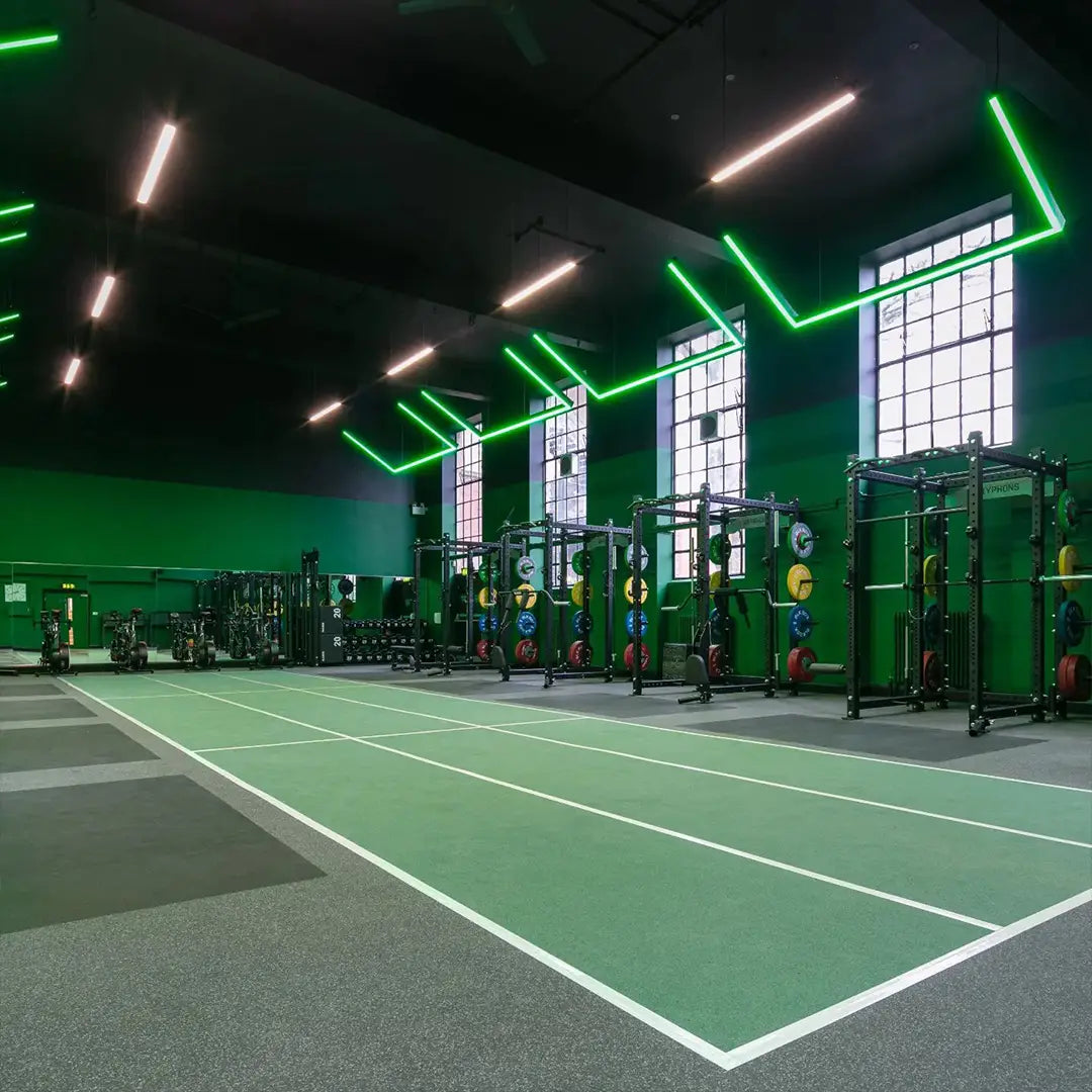 Large RGBW LED lights in a angular linear shape within a gym. The lights are set to green over the weights area.